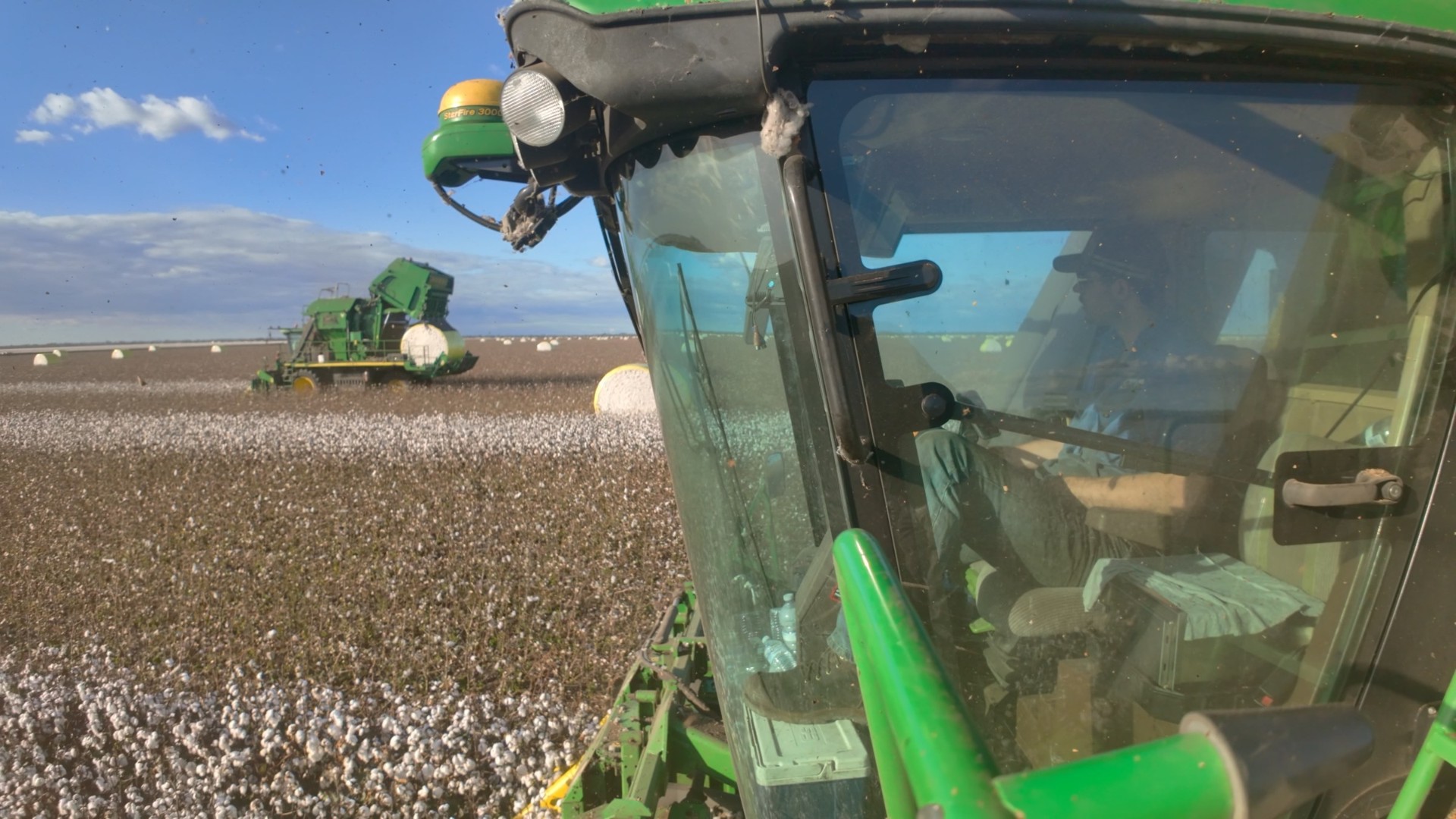 In-cab POV out the windscreen across a cotton field with a picker working ahead